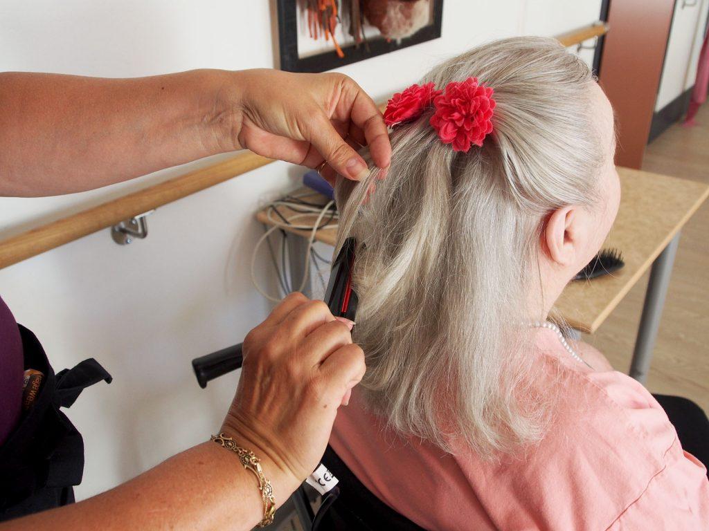 Hoitaja letittää asiakkaan hiuksia aamutoimien yhteydessä. Asiakkaan hiuksiin on laitettu upea punainen kukka.