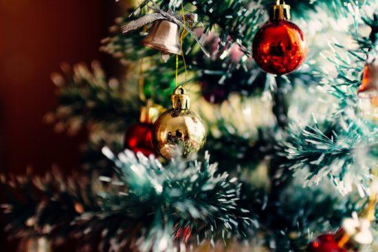 Kuvassa on joulukuusen kuusen oksia. Oksiin on kiinnitetty koristeita, palloja ja kelloja.