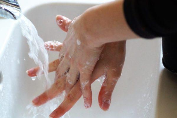 Lähikuva käsistä. Käsissä on saippuaa ja niitä pestään virtaavan veden alla.