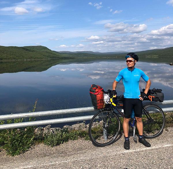Mika Riikonen seisoo pyörän edessä . Taustala on järvimaisema.