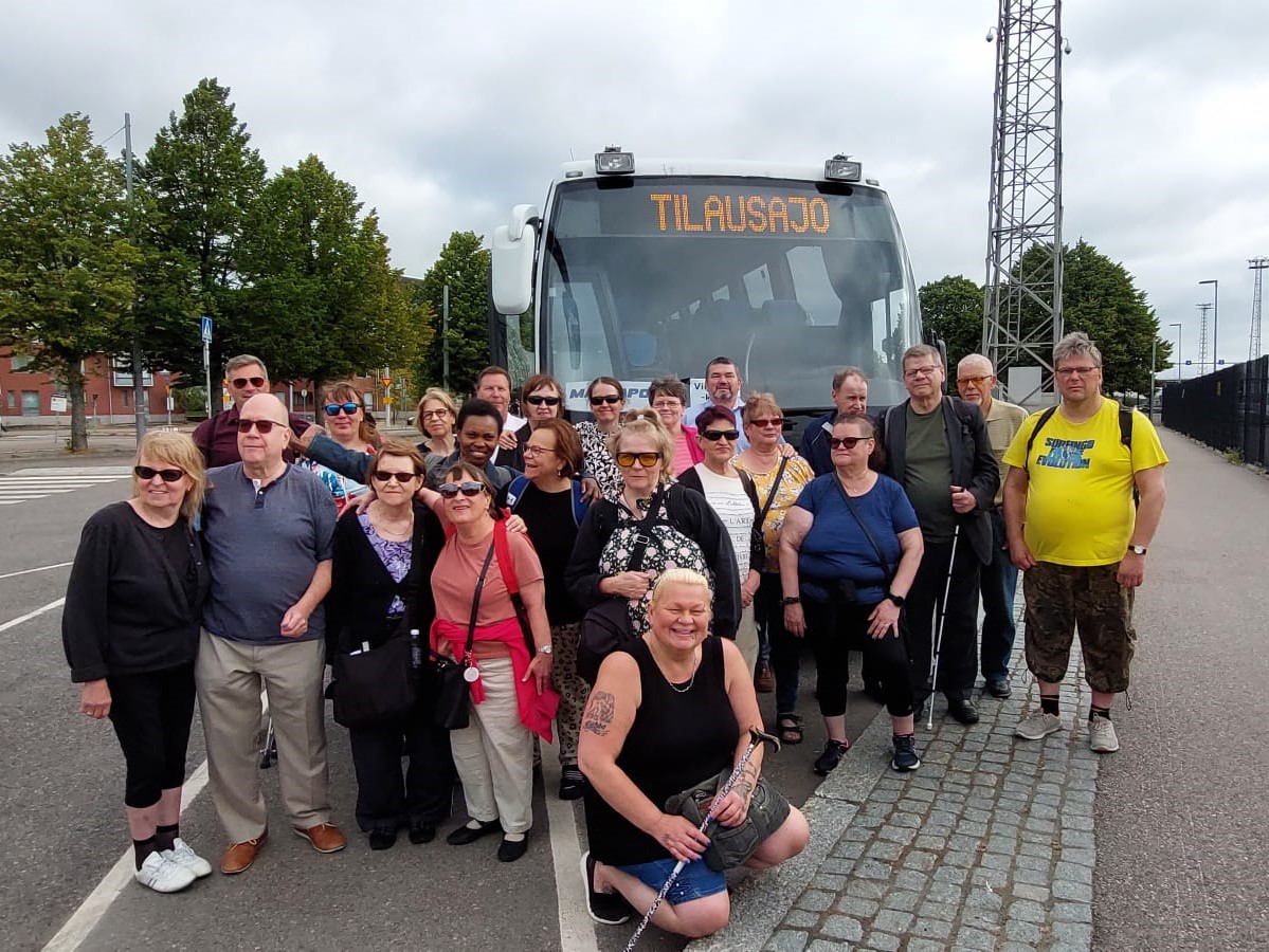 Viittojat kerholaisia ryhmäkuvassa. Taustalla bussi.