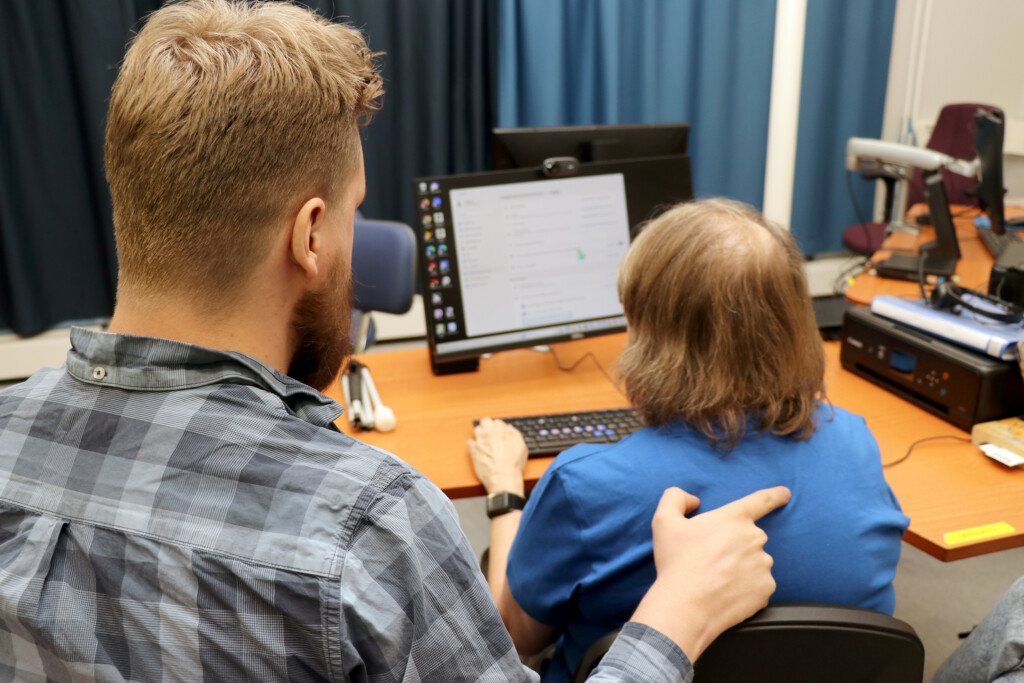 ICT kouluttaja ohjaa asiakasta tietokoneen käytössä, tehden kehomerkin.