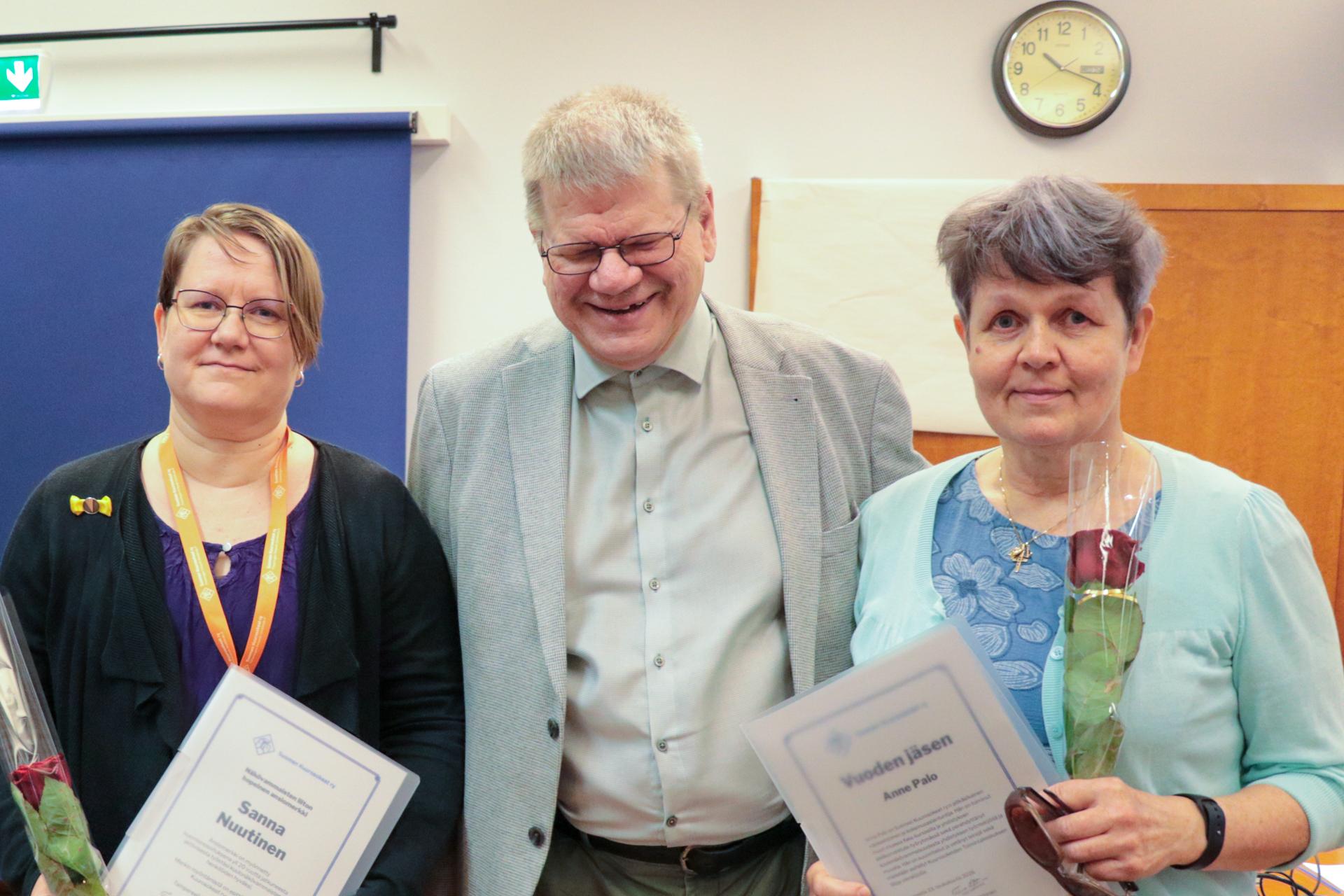Sanna Nuutinen, puheenjohtaja Timo Lehtonen ja Anne Palo. Sannalla ja Annella on käsissään kunniakirja ja ruusu.
